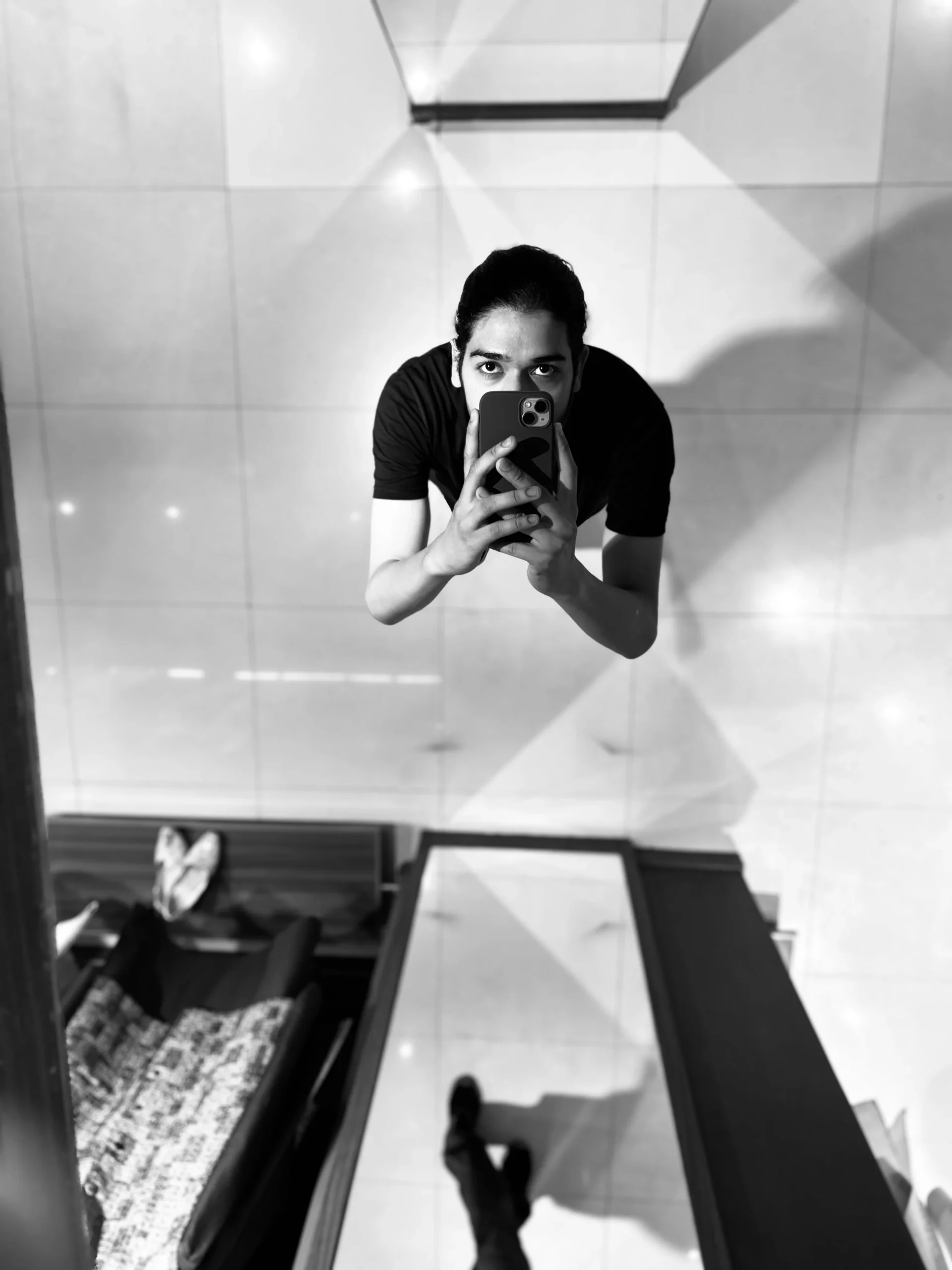 Black and white mirror shot of a man holding an iPhone, captured from a top-down perspective — conceptual photography by The Rose Camera