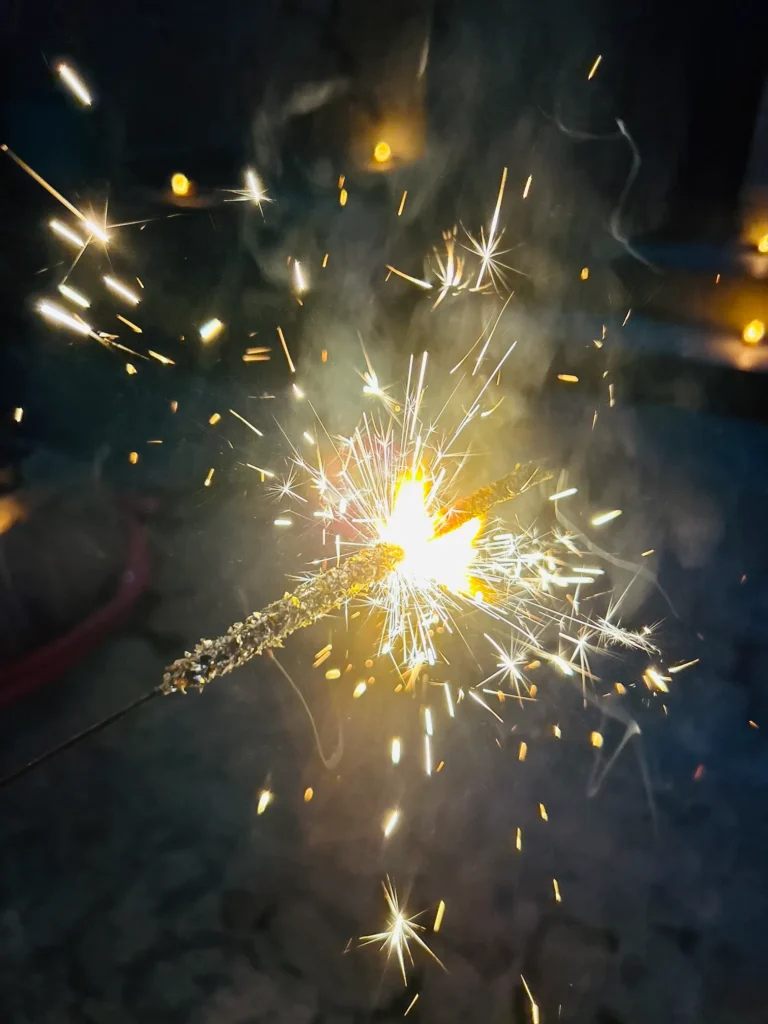 "A brightly lit sparkler emitting golden sparks and light in the dark during festive celebrations."